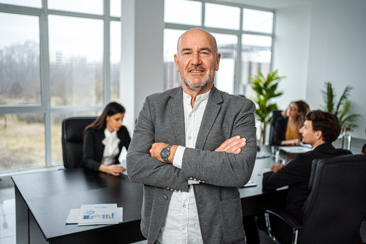 A senior executive standing in a boardroom with his team