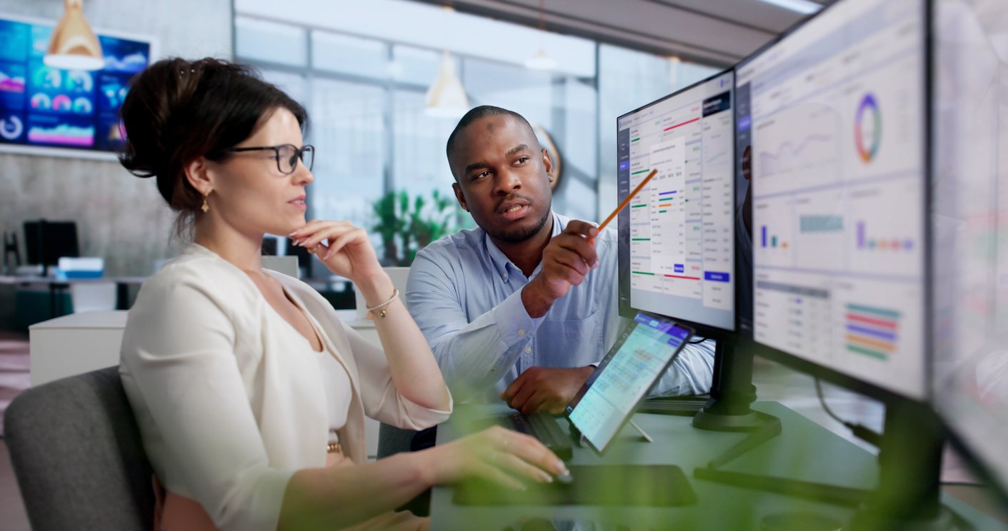 Two colleagues reviewing compliance dashboards together on screen